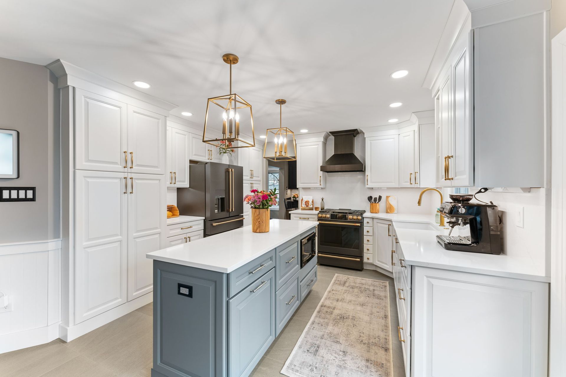 Bright white kitchen with blue island, gold pendant lights, stainless appliances, and a patterned runner rug In Newton PA