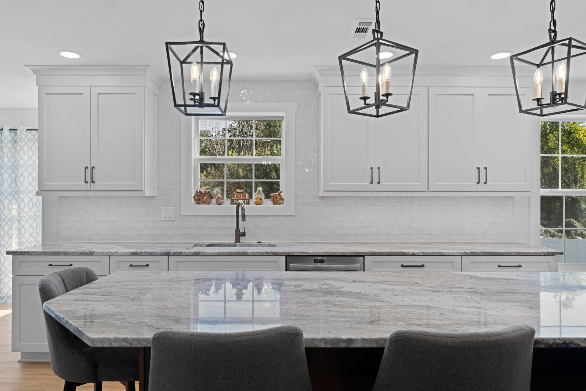 Bright modern kitchen with white cabinets, marble island, and three black pendant lights  In Bucks County PA