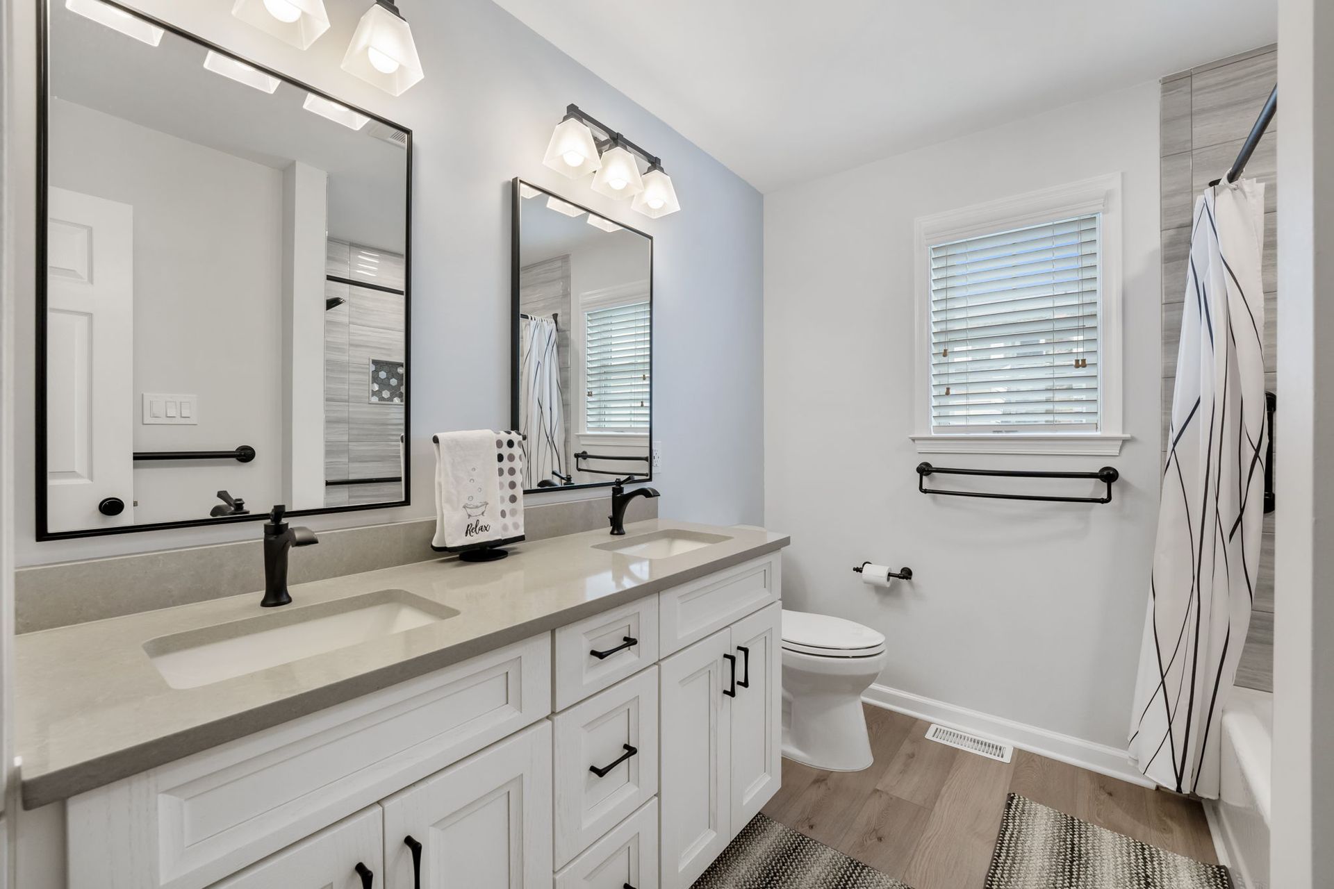 Bright white bathroom with double vanity, black mirrors, toilet, shower curtain, and small window  In Bucks County PA