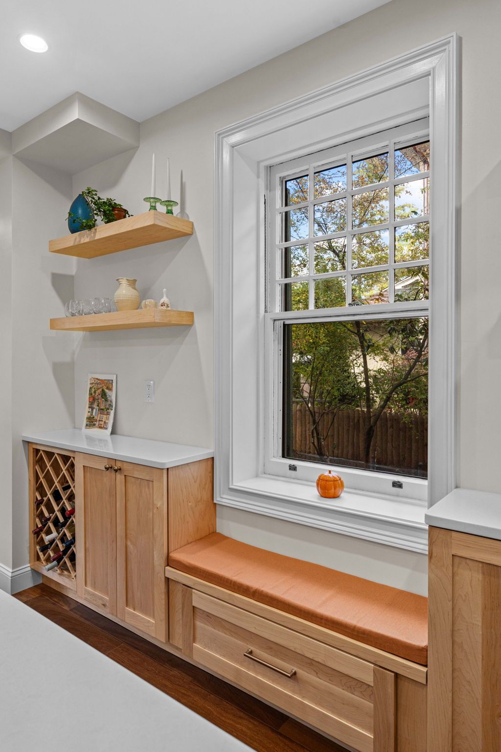 Built-in window seat with orange cushion, wood storage drawers, and floating shelves in a bright room In Bucks County PA