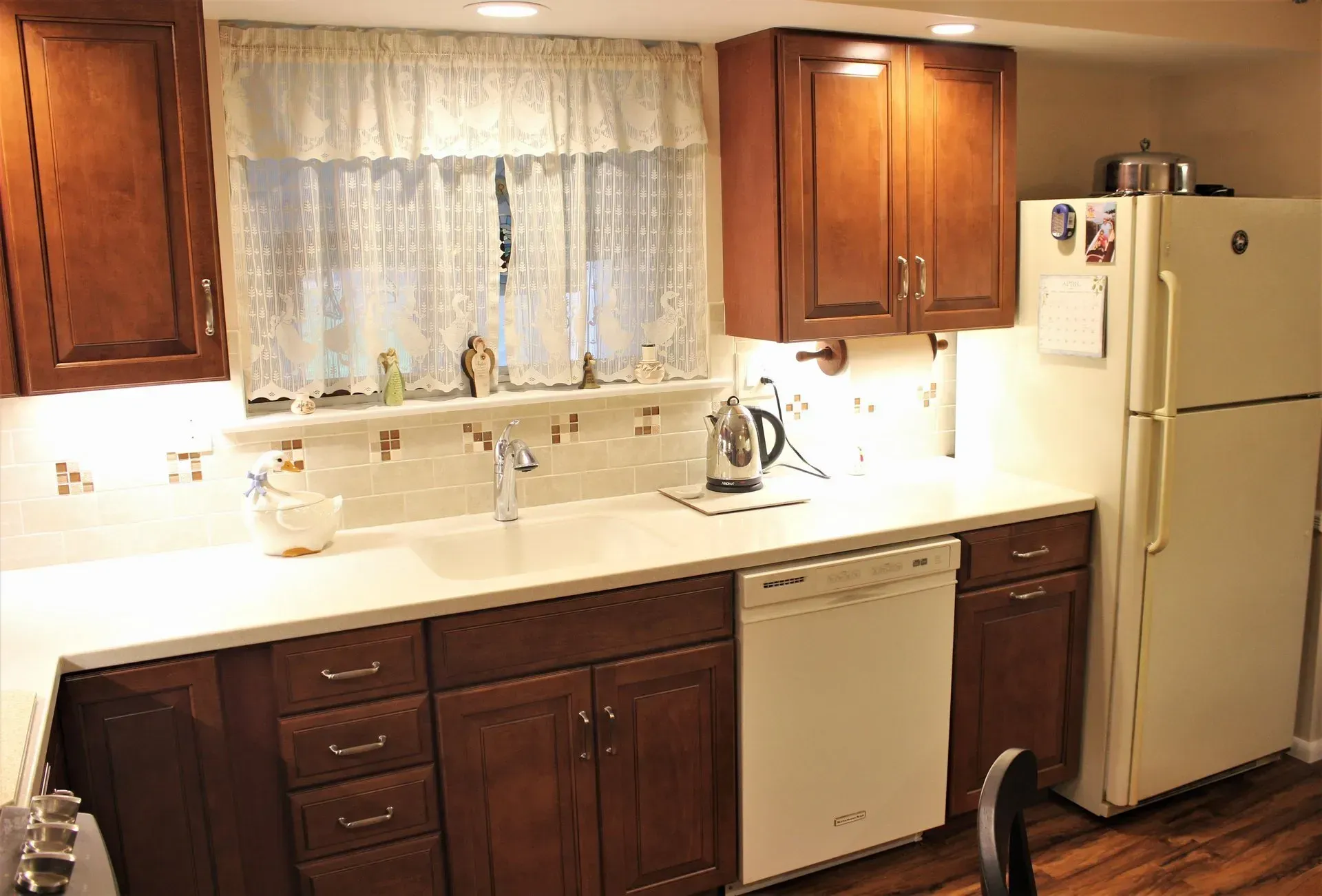 Compact kitchen with dark wood cabinets, white countertops, sink under a window, dishwasher, and white fridge In Bucks County PA