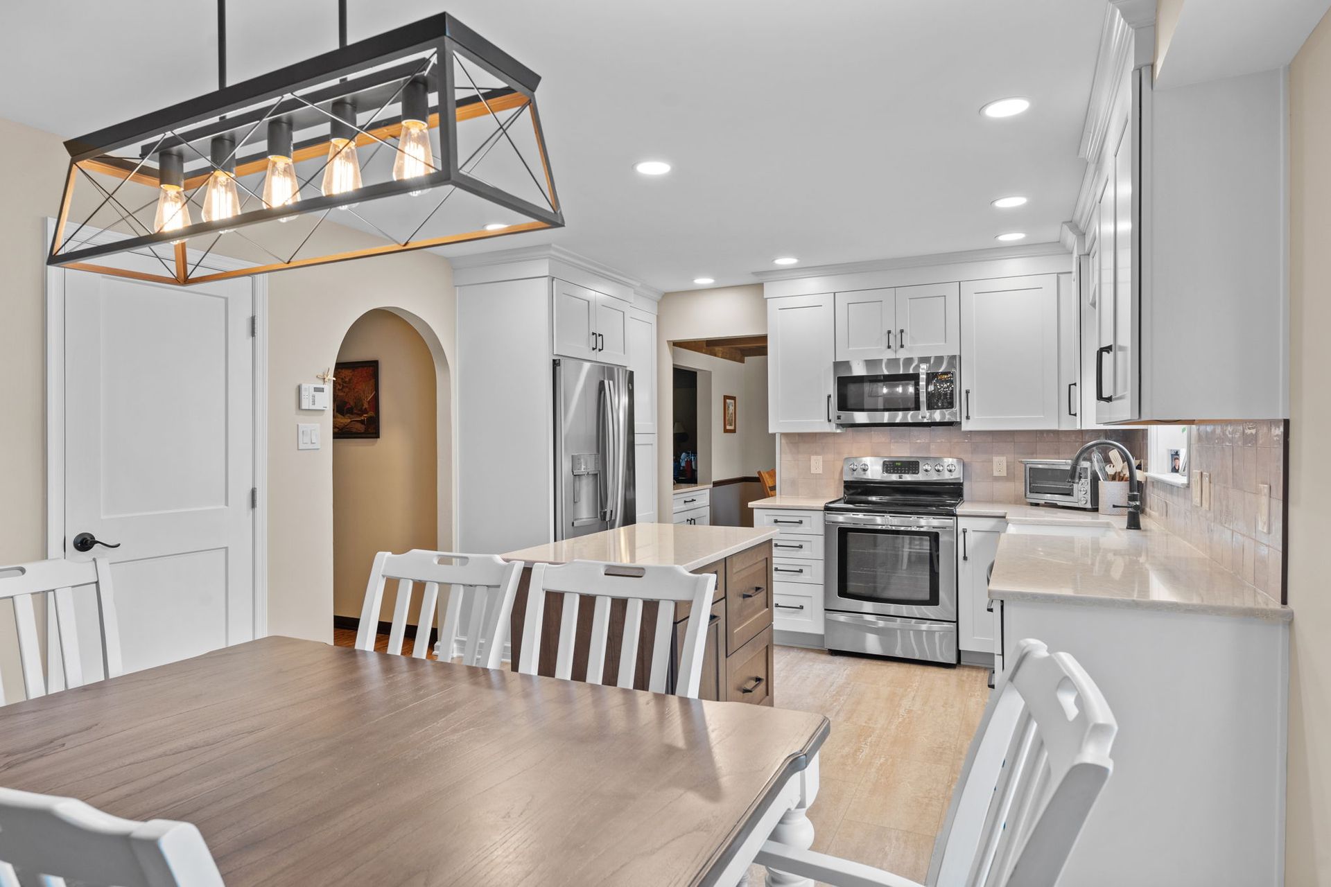 Bright modern kitchen and dining area with white cabinets, stainless appliances, and wood table under pendant light  In Bucks County PA