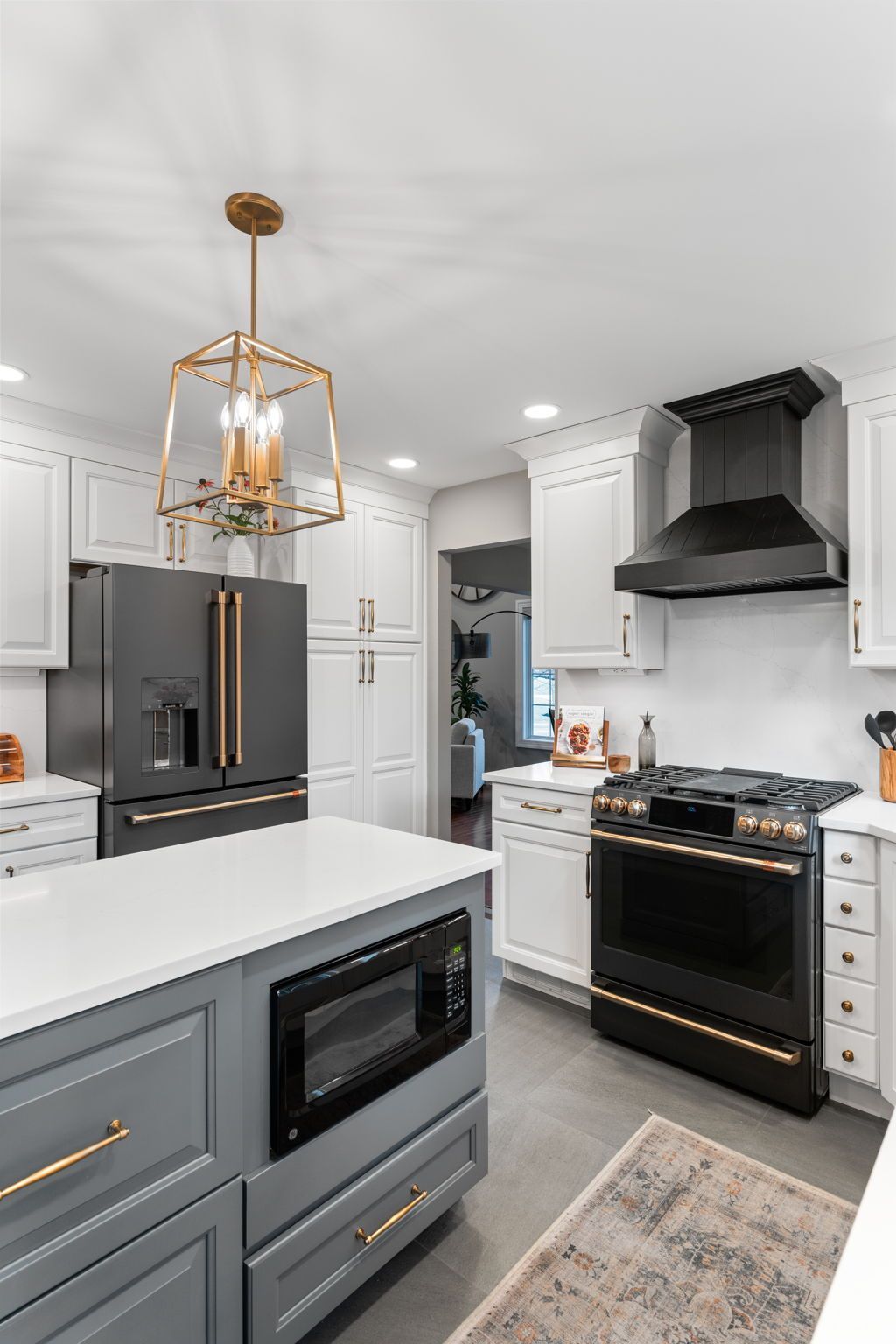 Modern white kitchen with black appliances, gray cabinets, gold pendant light, and island with microwave In Bucks Country PA