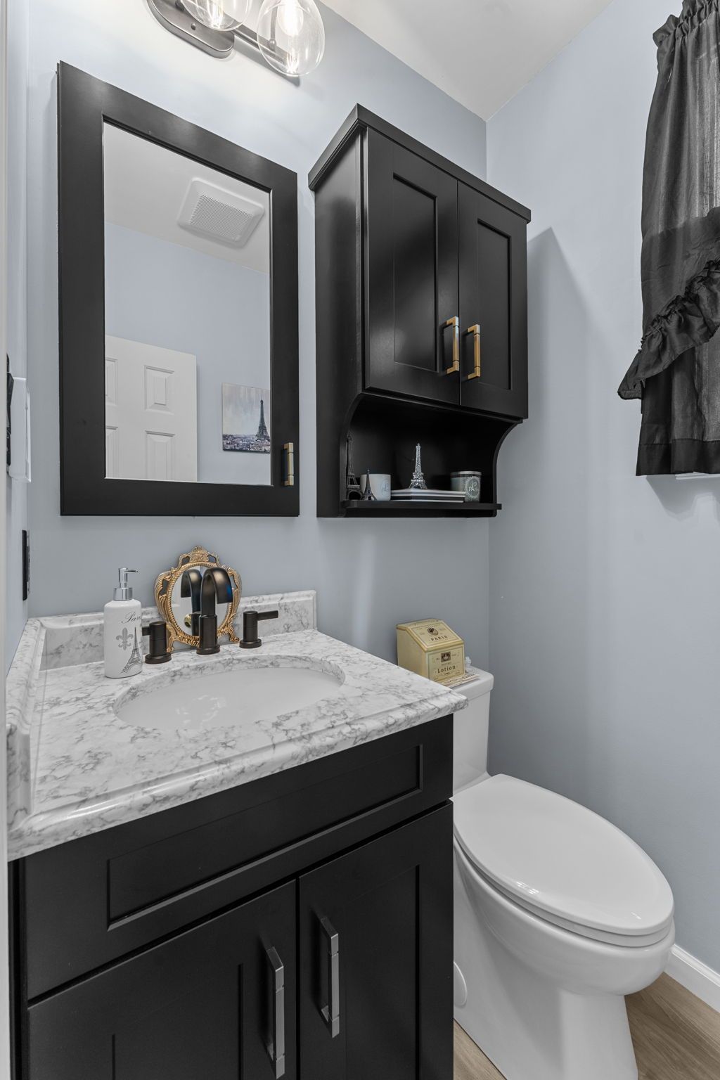 Small bathroom vanity with black cabinet, marble countertop, mirror, and toilet beside a wall cabinet In Bucks Country PA