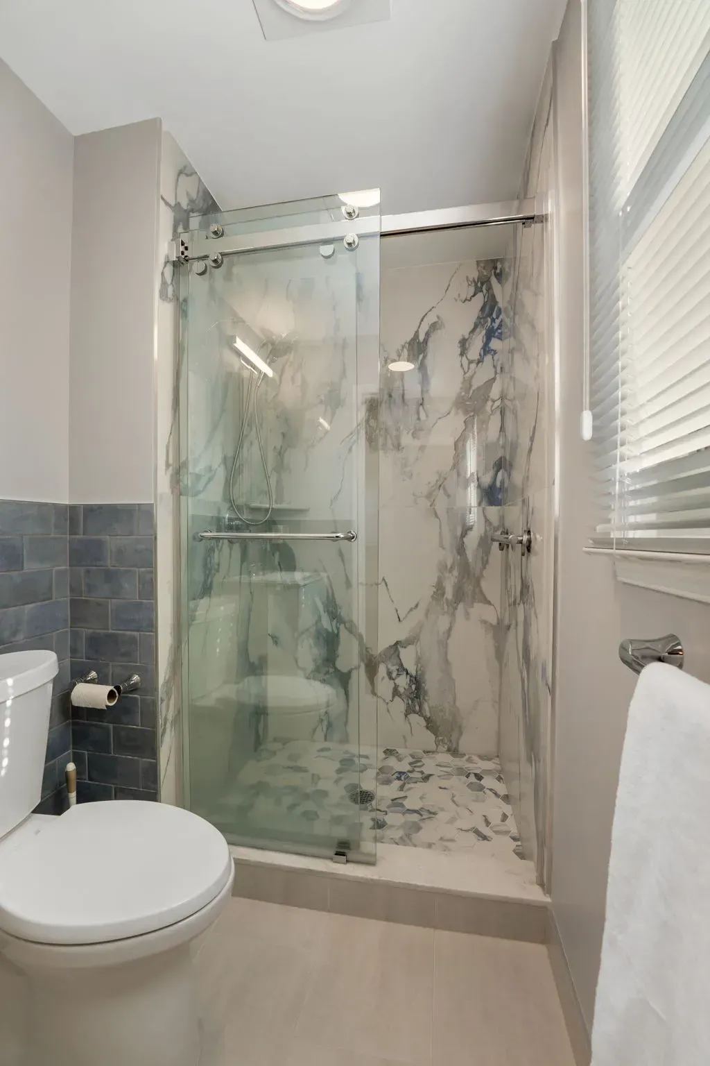 Small bathroom with glass shower enclosure, marble-look walls, toilet, and window blinds  In Bucks County PA