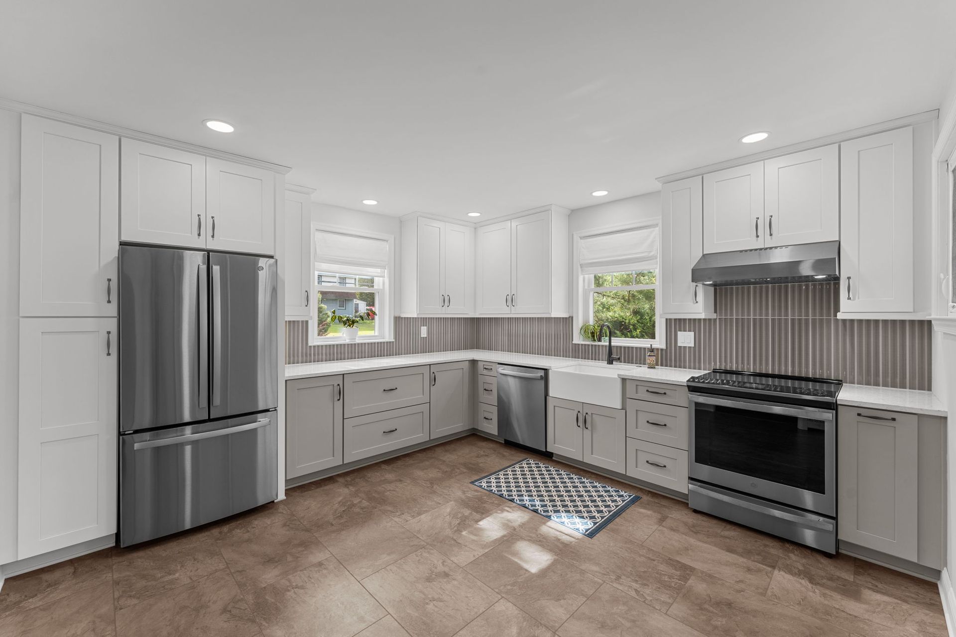 Bright modern kitchen with white cabinets, stainless steel appliances, gray countertops, and a tiled floor In Bucks County PA