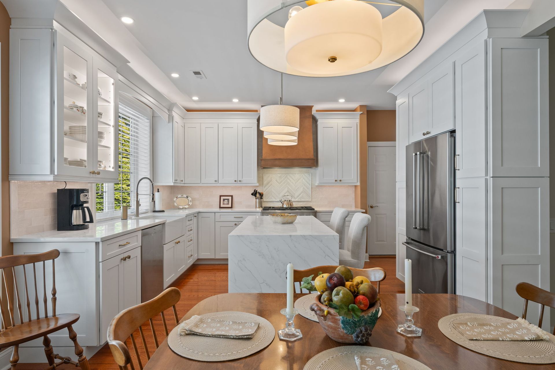 Bright, modern white kitchen with island, stainless fridge, wooden table, and fruit centerpiece In Bucks County PA