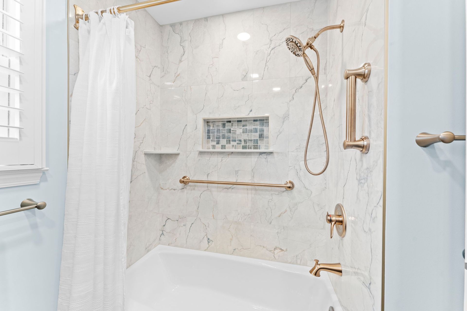 Accessible white marble shower with gold grab bars, handheld shower, and bench seating In Bucks County PA