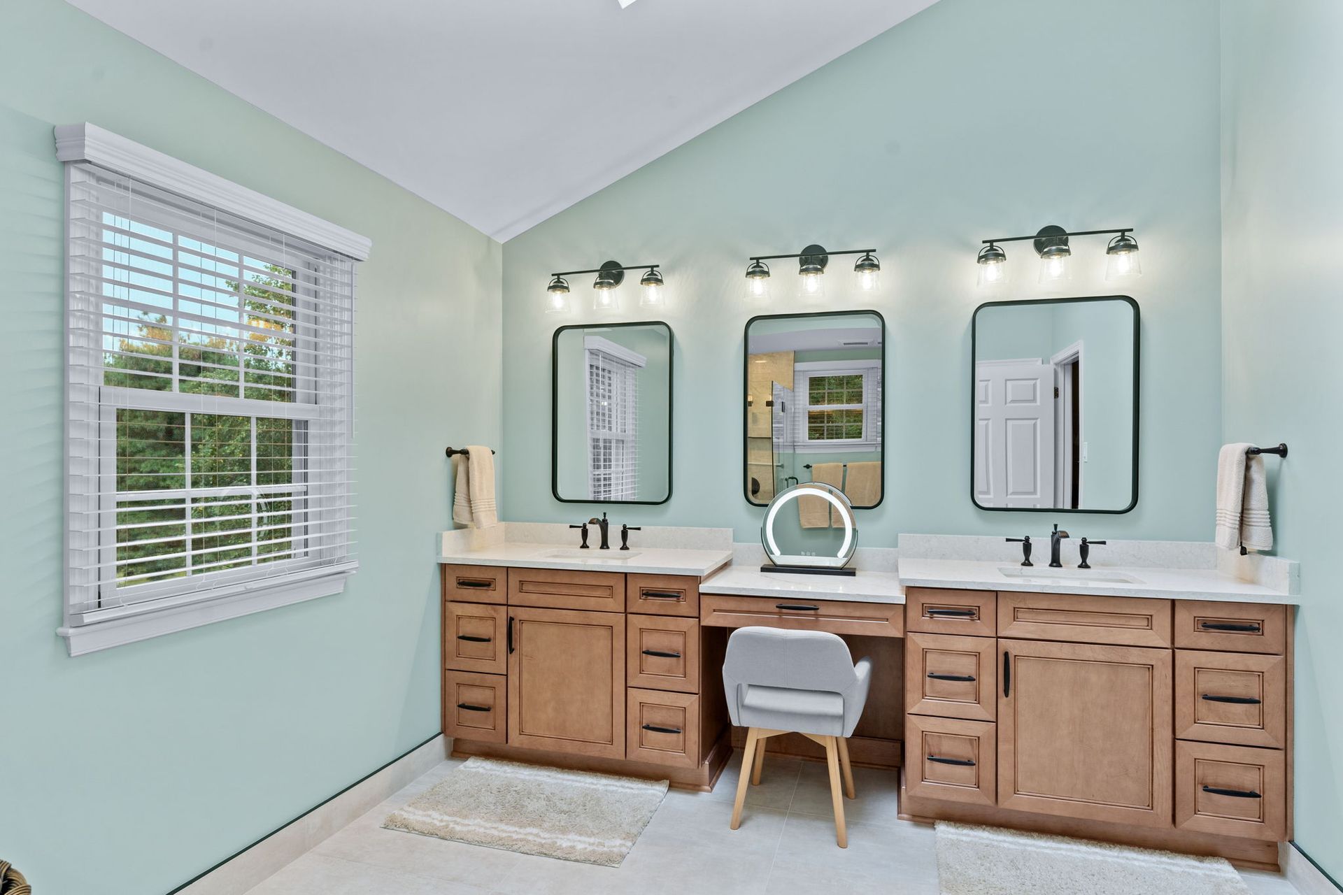 Light aqua bathroom with dual wooden vanities, mirrors, and a central stool In Bucks County PA