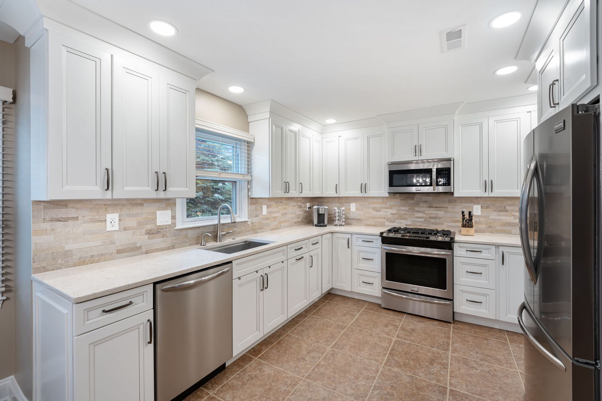 Bright modern white kitchen with stainless steel appliances, tile backsplash, and large window In Bucks County PA