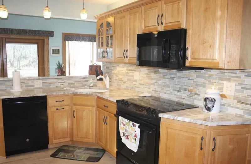 Small kitchen with wood cabinets, black appliances, granite countertops, and pendant lights In Bucks Country PA