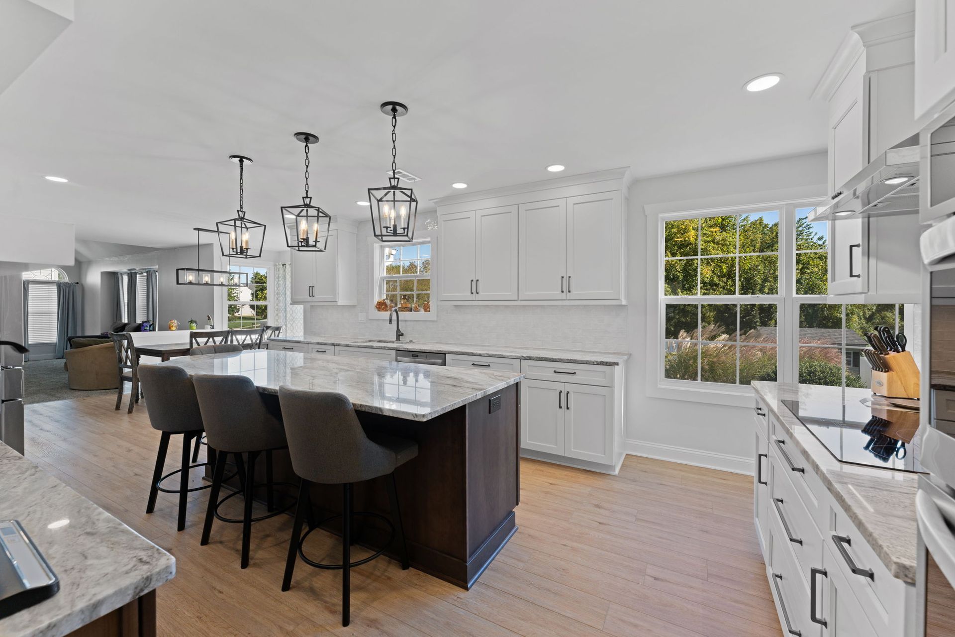 Bright modern kitchen with island, black bar stools, pendant lights, white cabinets, and large window  In Bucks County PA