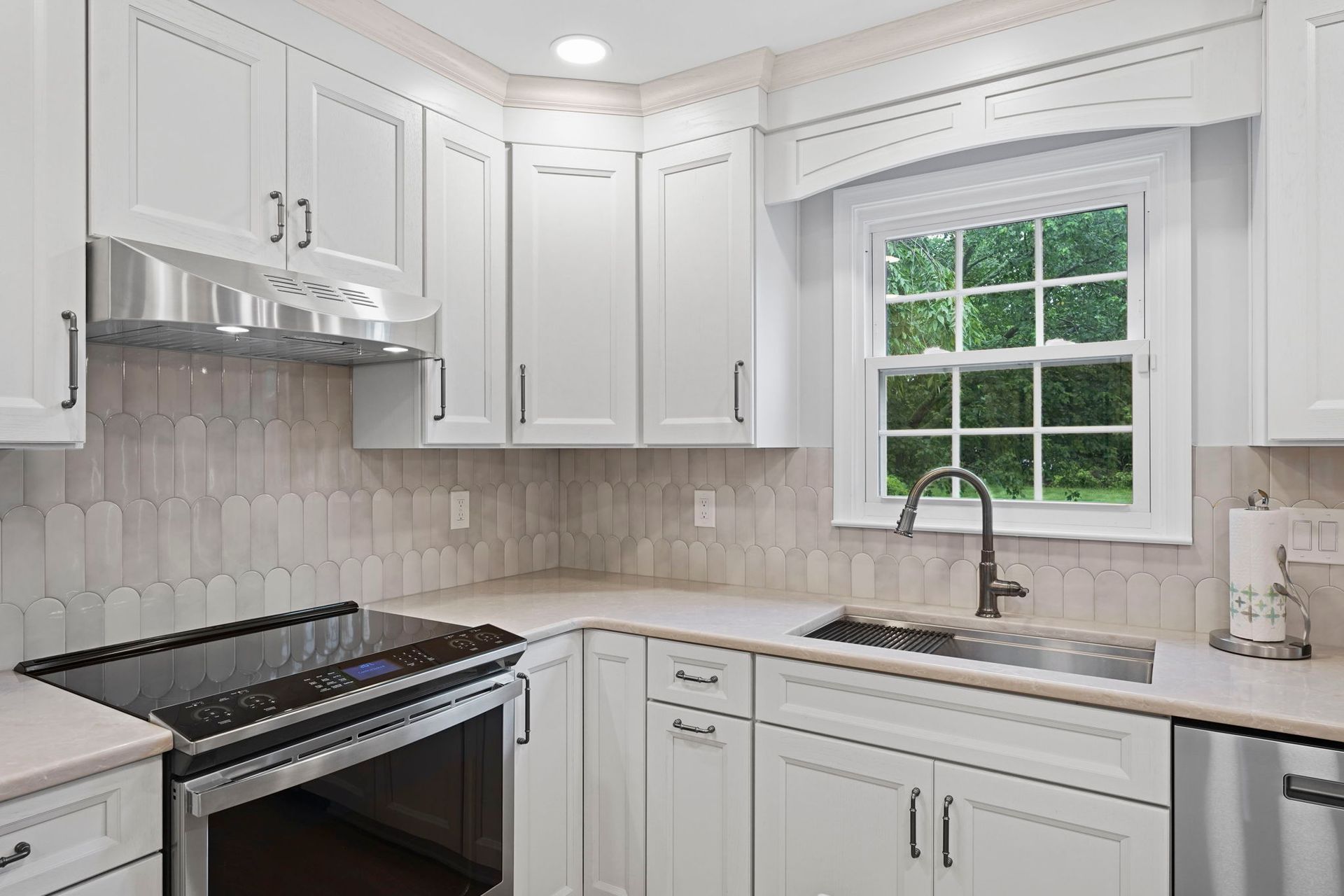 Bright white kitchen with cabinets, black stove, tiled backsplash, and a window over the sink in Bucks County PA