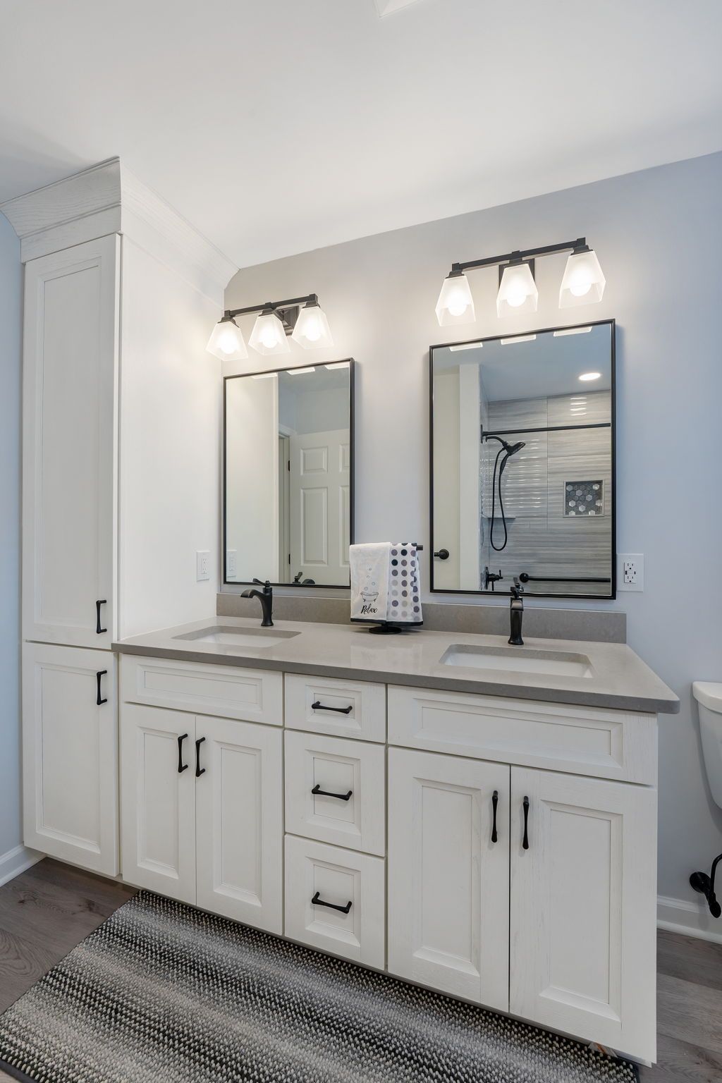 White bathroom vanity with double mirrors, black faucets, and wall sconces above a striped rug In Bucks County PA
