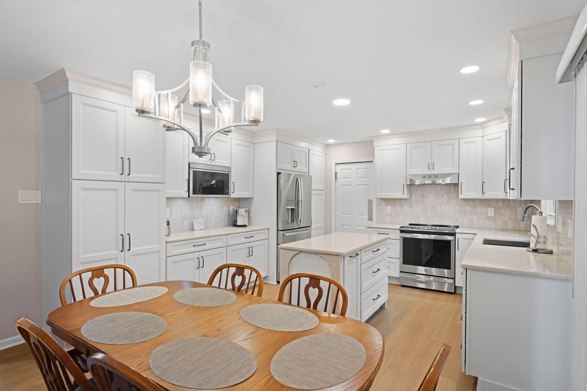 Bright white kitchen with island, chandelier, and round dining table on hardwood floor in Bucks County PA