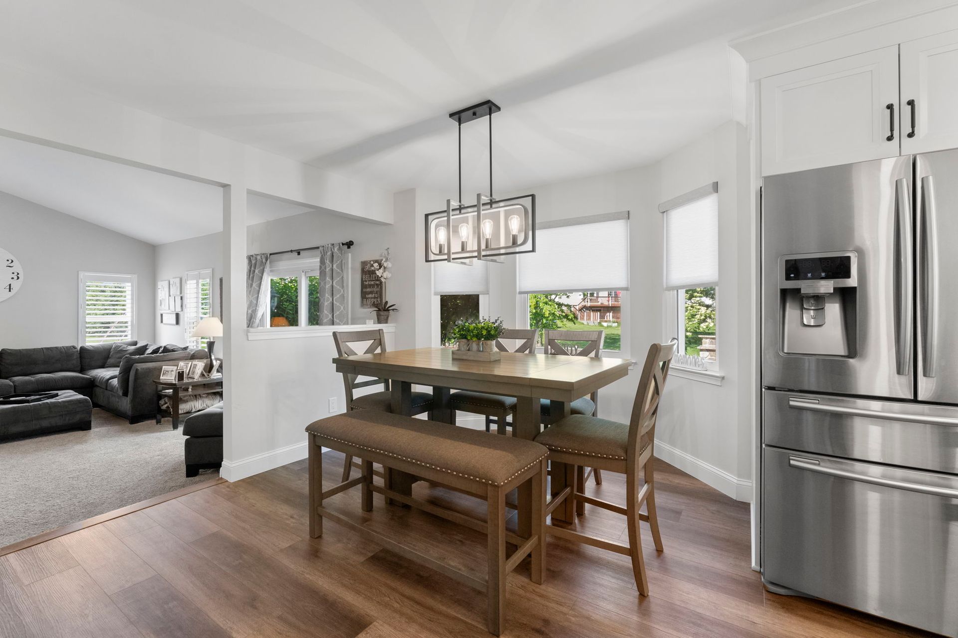Bright kitchen and dining area with wood table, bench, stainless steel fridge, and open view to living room In Bucks County PA