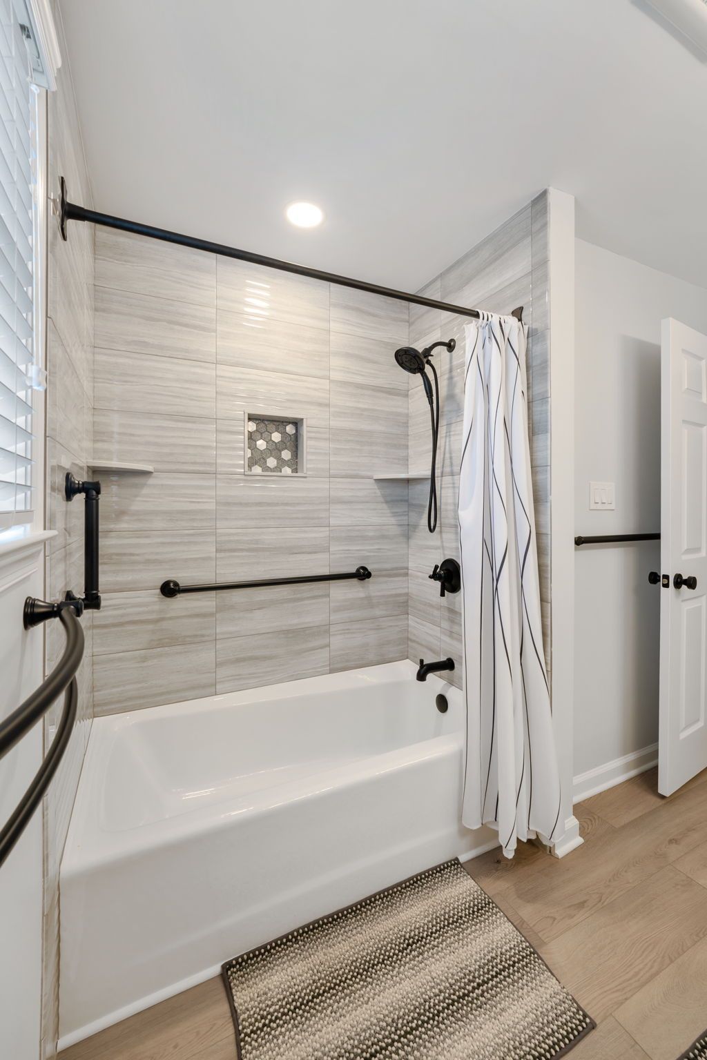 Accessible bathroom with white tub, black grab bars, shower curtain, and striped rug In Bucks County PA