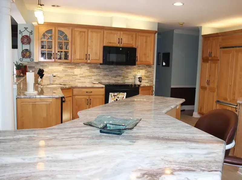 Modern kitchen with wood cabinets, stone island, black appliances, and a dining chair in the foreground in Washington 