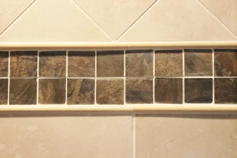 Beige tiled wall with a horizontal strip of dark stone mosaic tiles between sections  In Bucks County PA