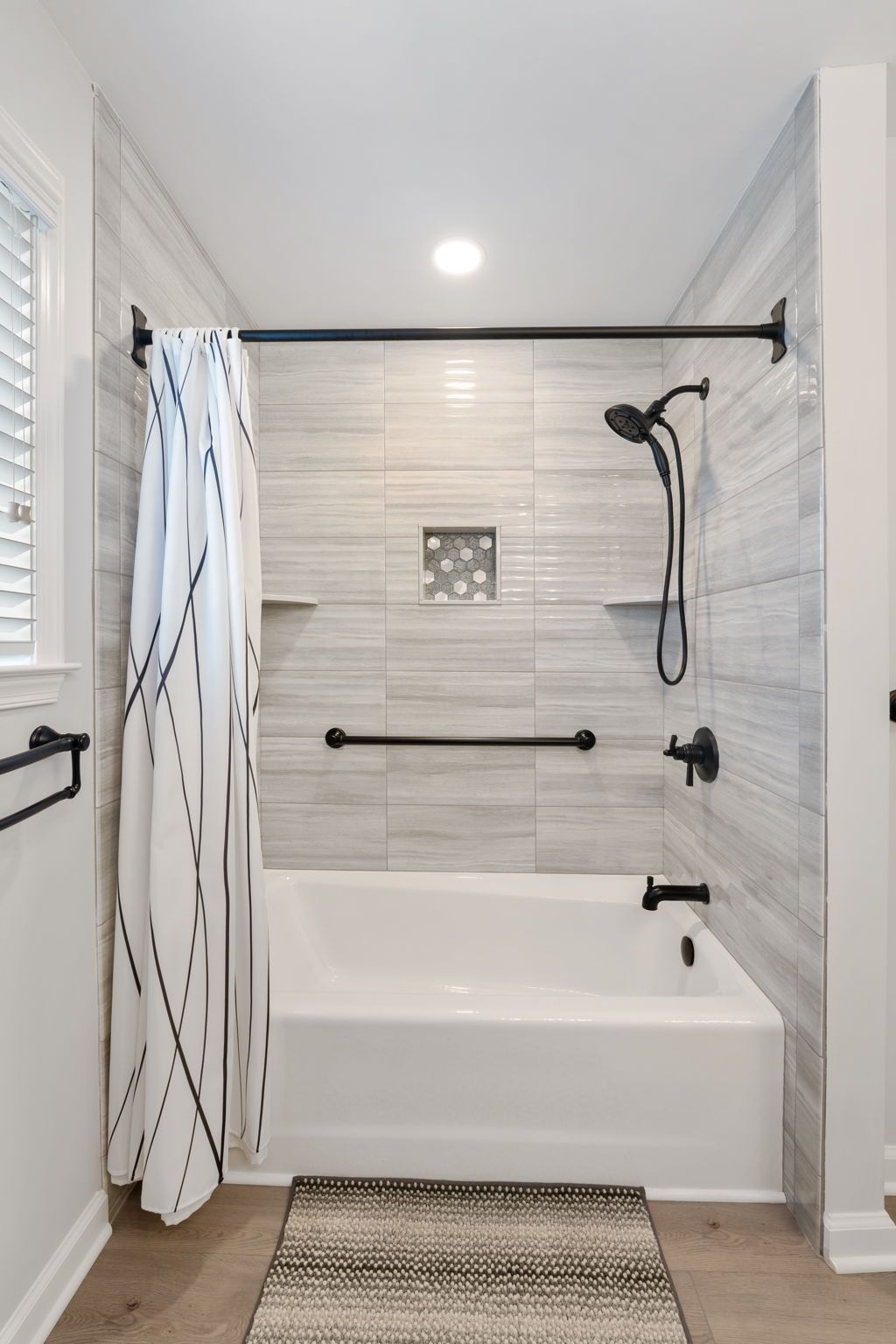Accessible white-tiled bathtub and shower with grab bars, curtain, and handheld showerhead In Bucks County PA