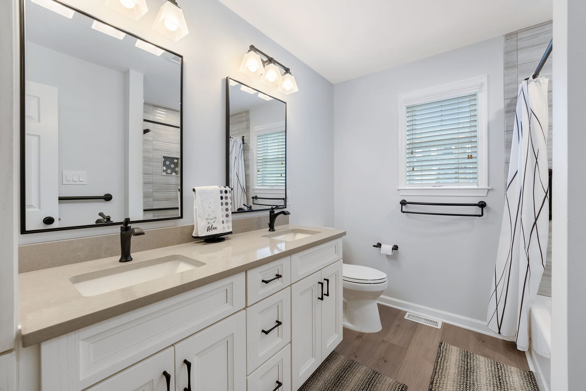 Bright bathroom with double vanity, mirrors, toilet, window, and shower curtain In Bucks County PA