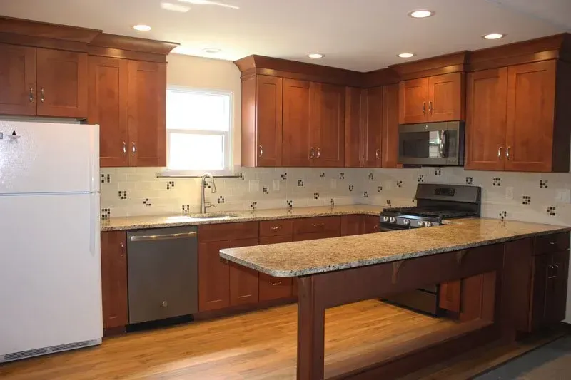 Kitchen with wood cabinets, white appliances, granite island, and a dishwasher under a window.In Bucks Country PA