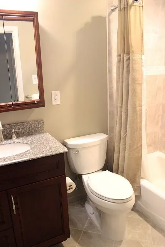 Small bathroom with vanity, toilet, and shower curtain in beige tones  In Bucks County PA