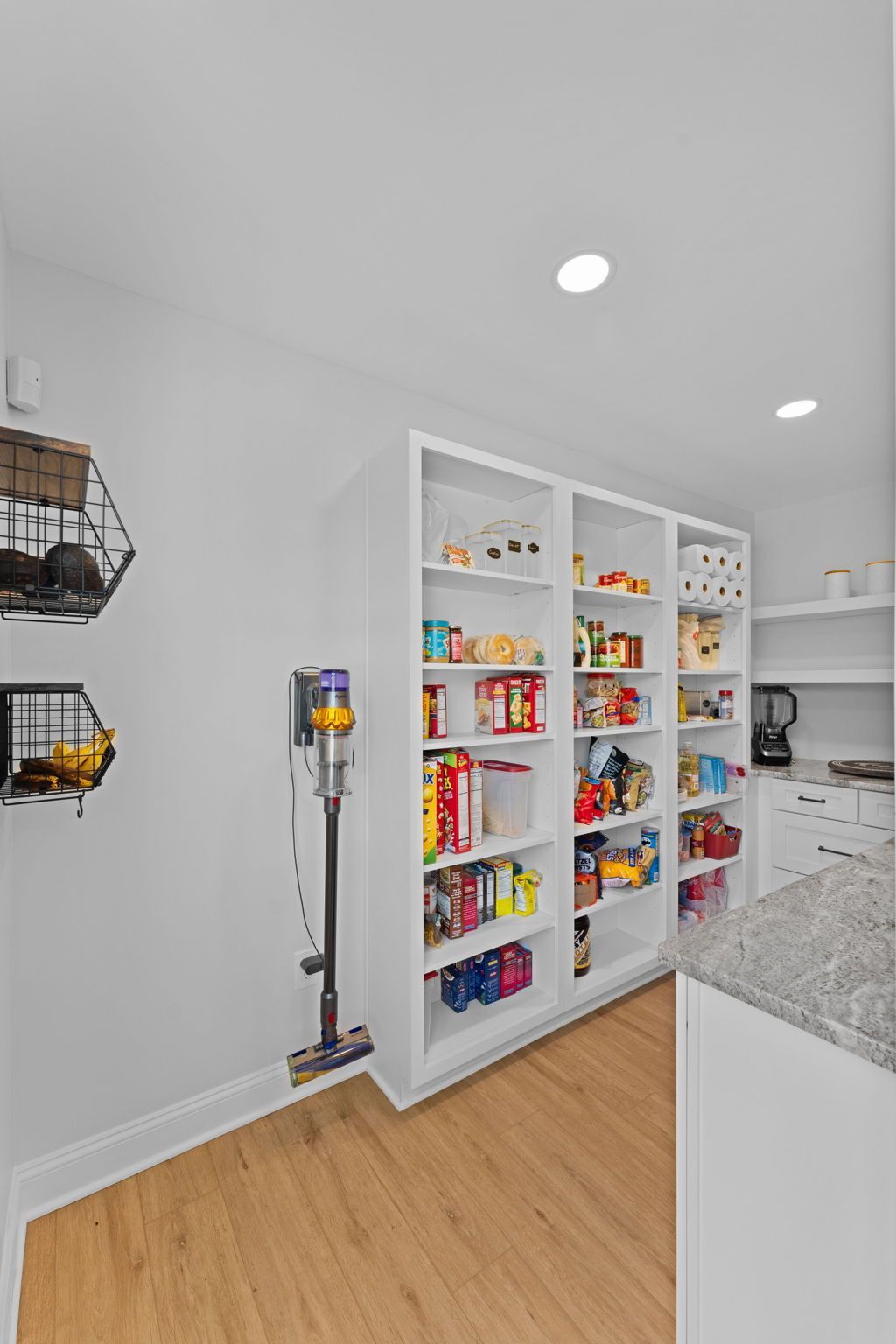 Pantry with white shelves stocked with food and snacks beside a kitchen counter and wood floor  In Bucks County PA