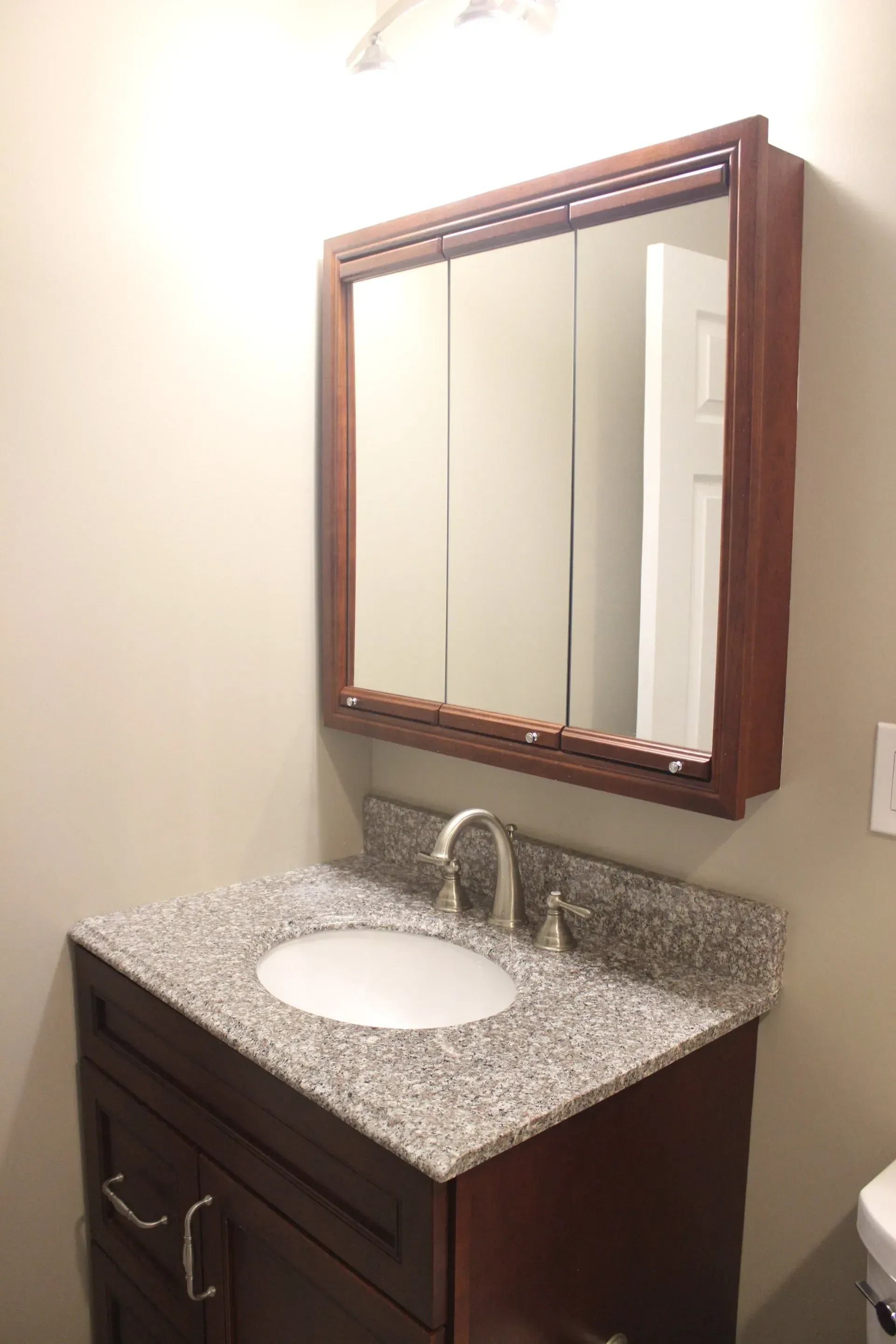 Bathroom vanity with speckled countertop, oval sink, wood cabinet, and wall mirror under warm light  In Bucks County PA
