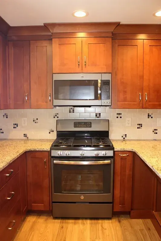 Compact kitchen with wood cabinets, stainless steel stove and microwave, cream tile backsplash, and granite counters  In Bucks County PA