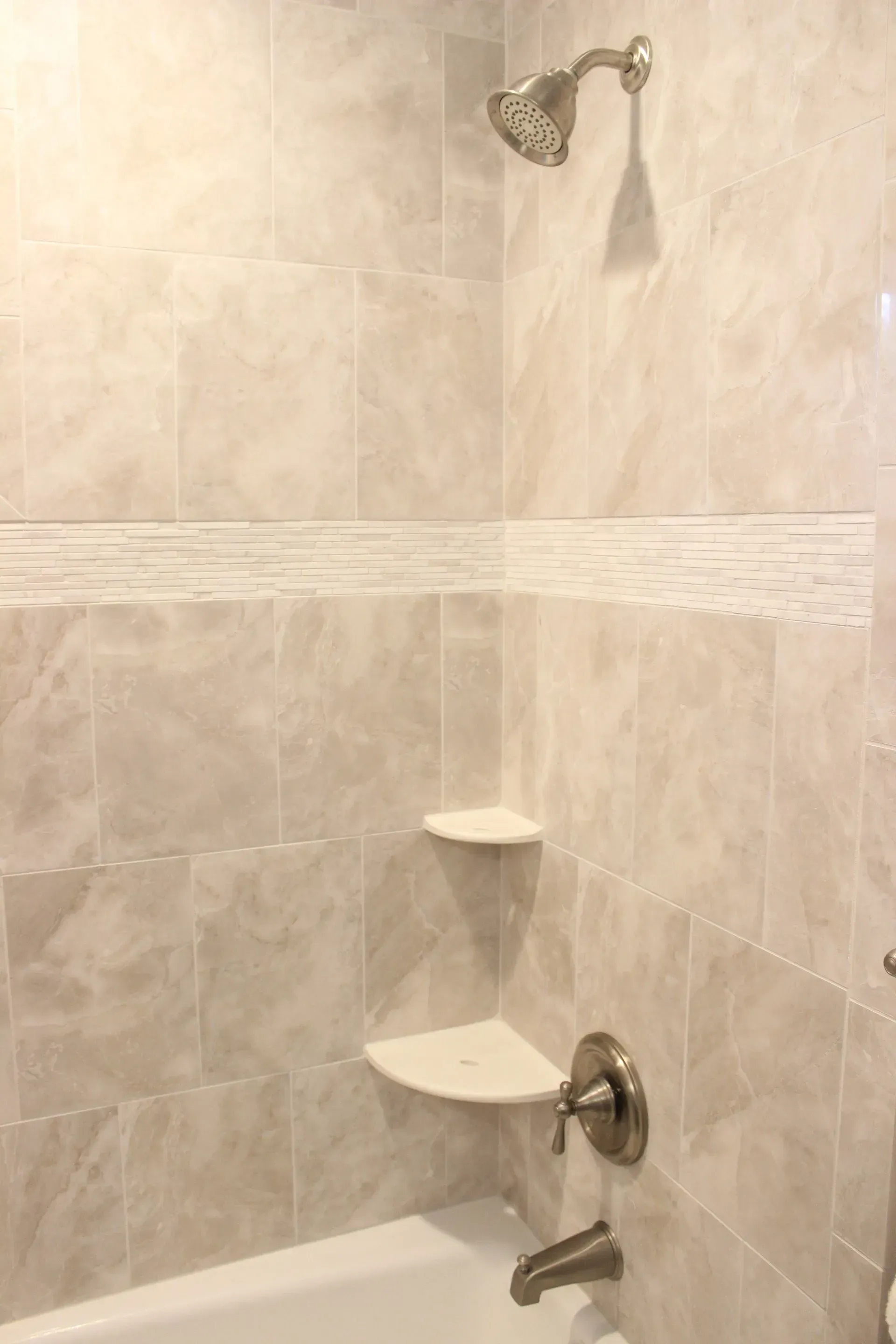 Shower stall with beige tile, wall-mounted showerhead, corner shelves, and grab bar  In Bucks County PA