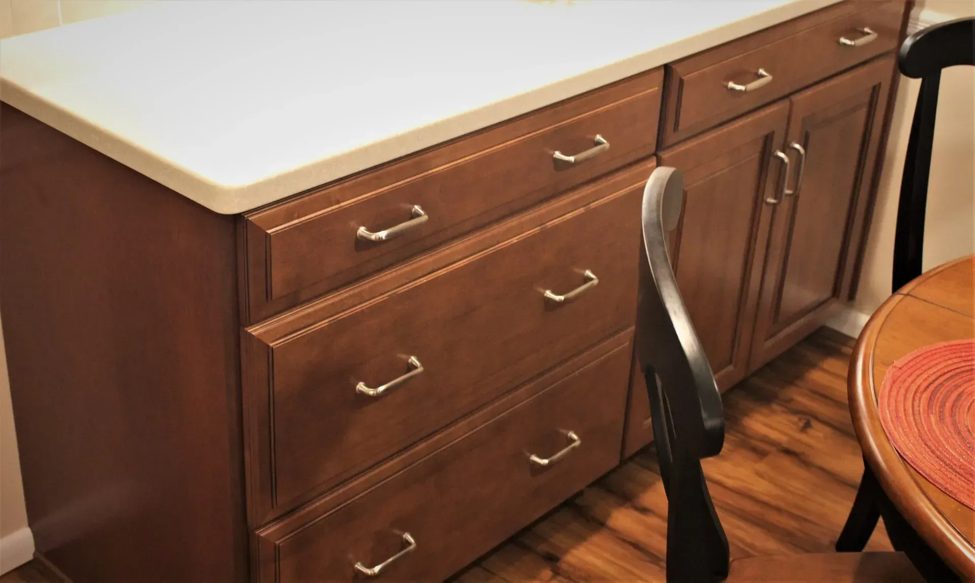 Wooden kitchen cabinets with drawers and a light countertop beside a chair and round table In Bucks County PA