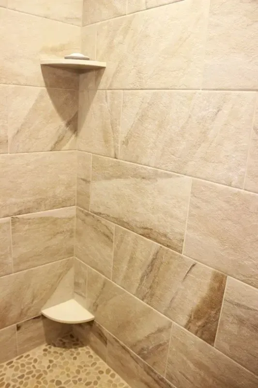 Tiled shower corner with two built-in corner shelves and beige stone-like walls In Bucks Country PA