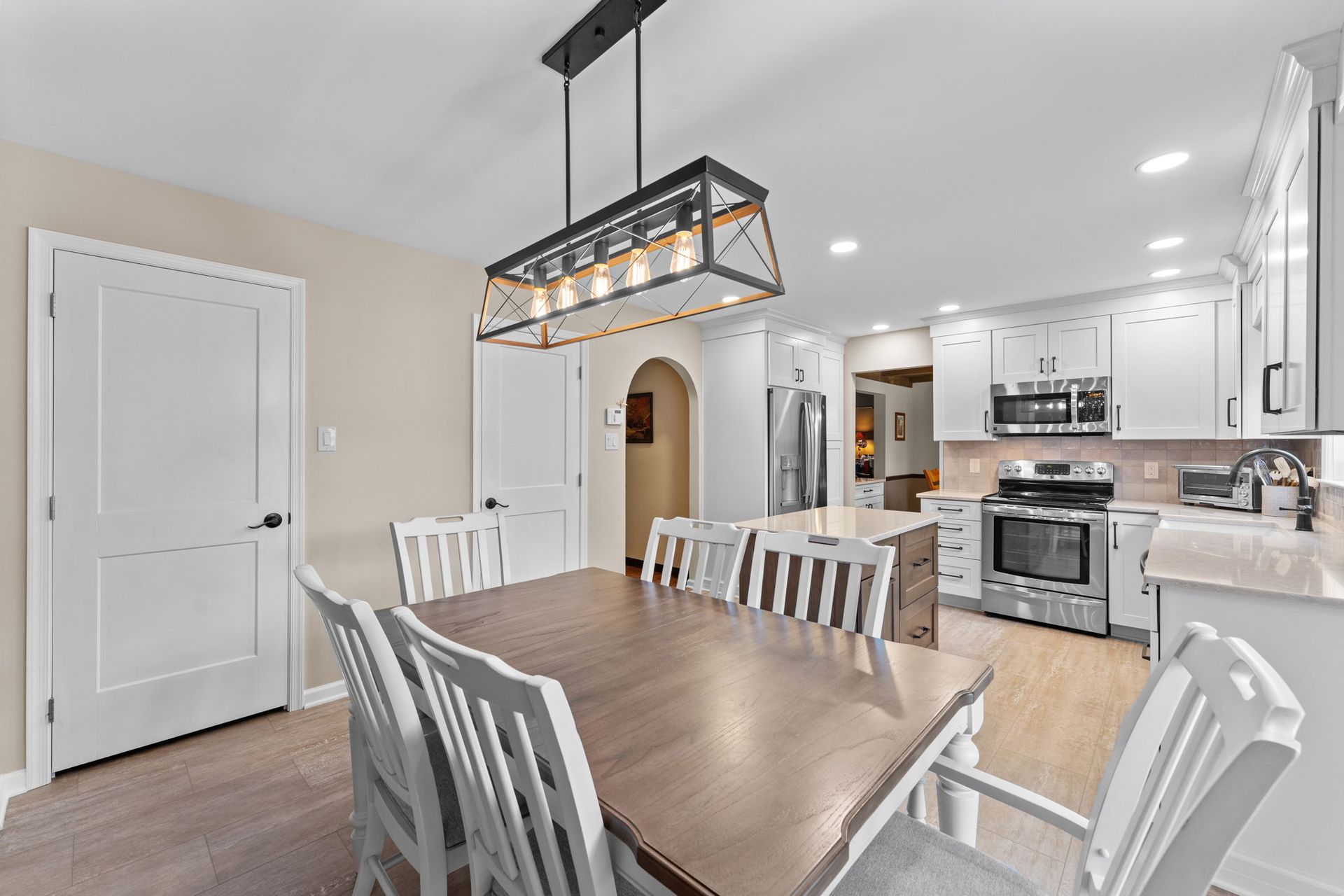 Bright kitchen with a wooden dining table, white chairs, stainless appliances, and a hanging light fixture  In Bucks County PA