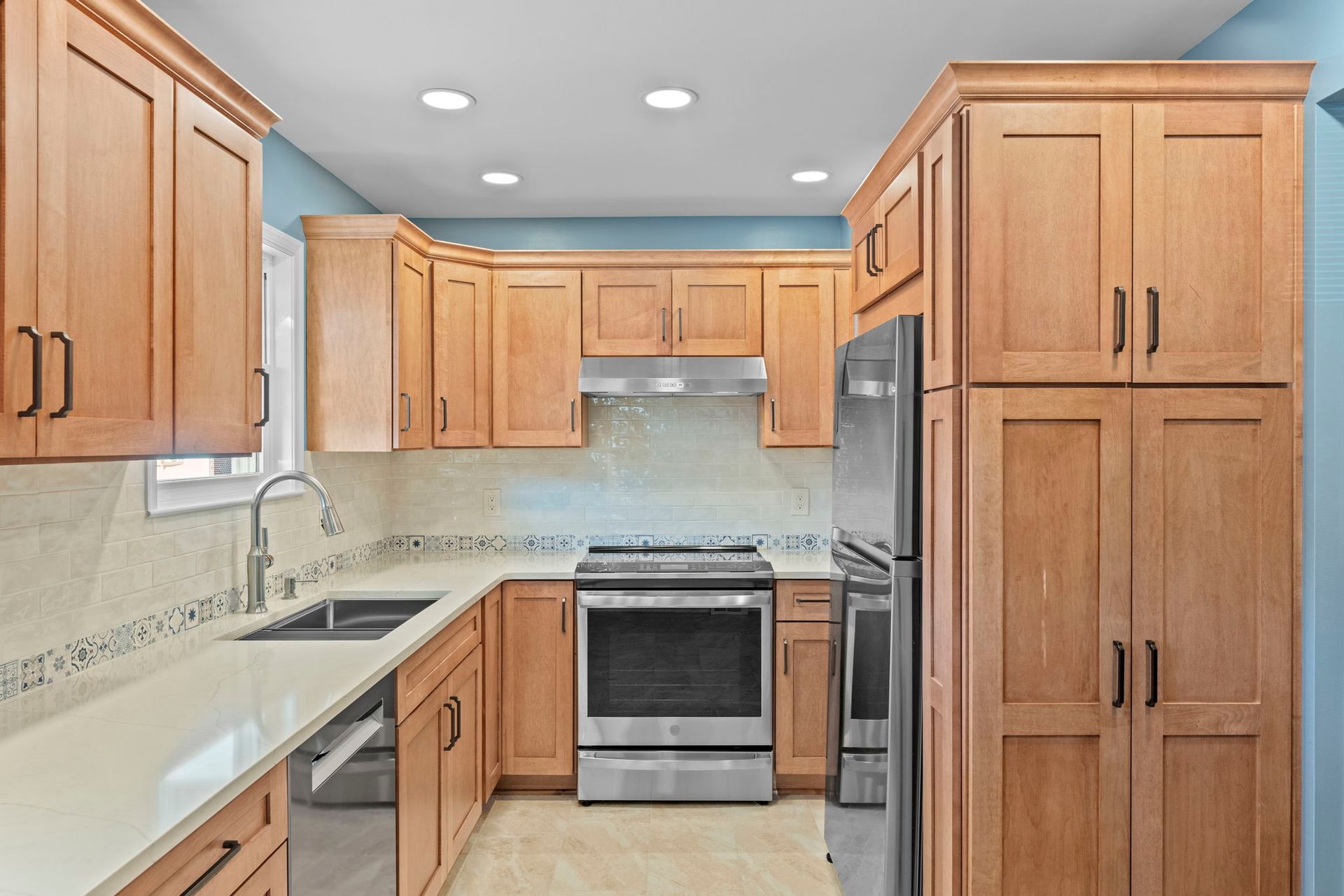 Modern kitchen with light wood cabinets, stainless steel stove, white countertops, and recessed ceiling lights In Bucks Country PA