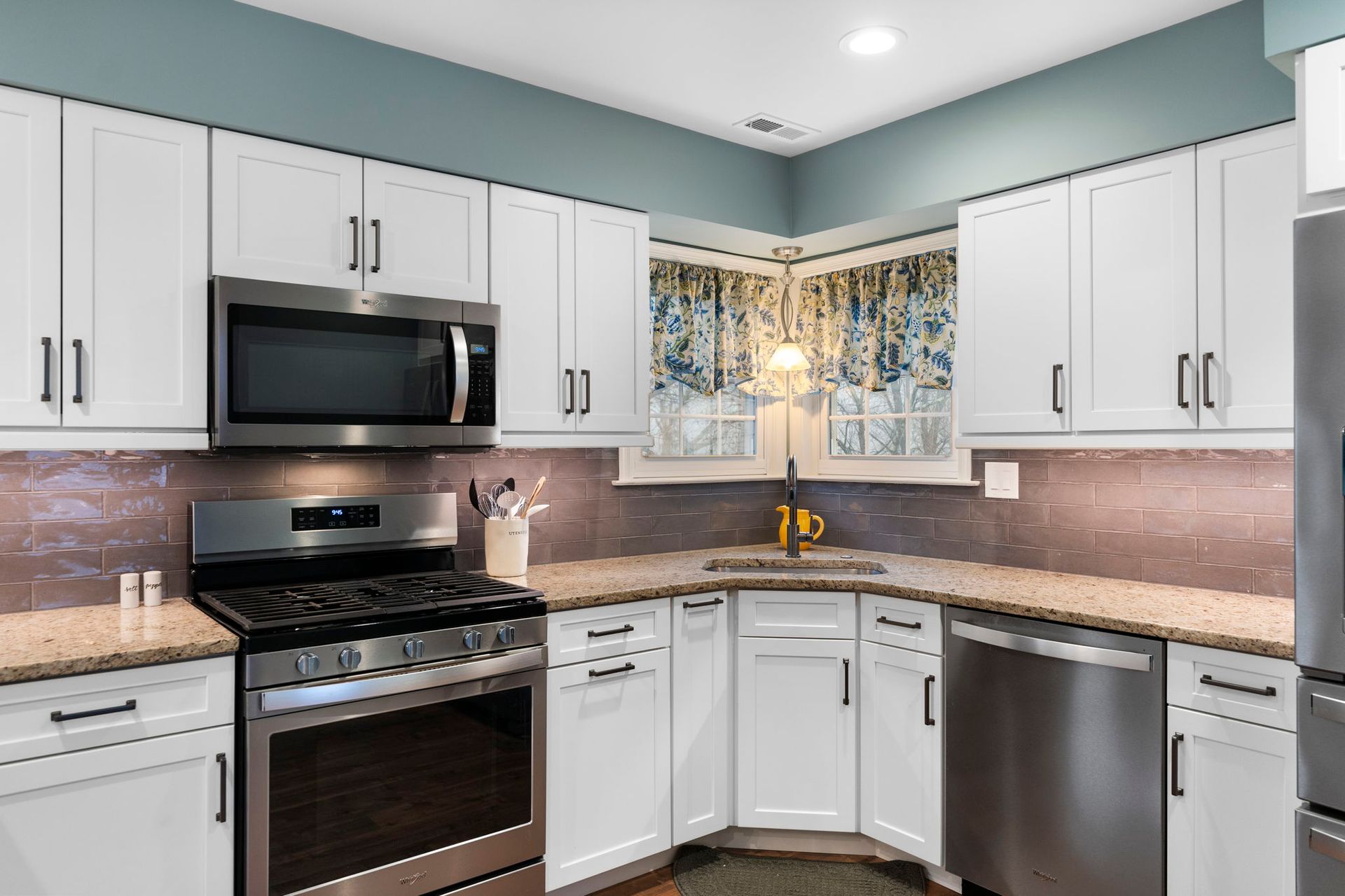 Modern kitchen with white cabinets, stainless appliances, black stove, and pink backsplash under a window In Bucks Country PA