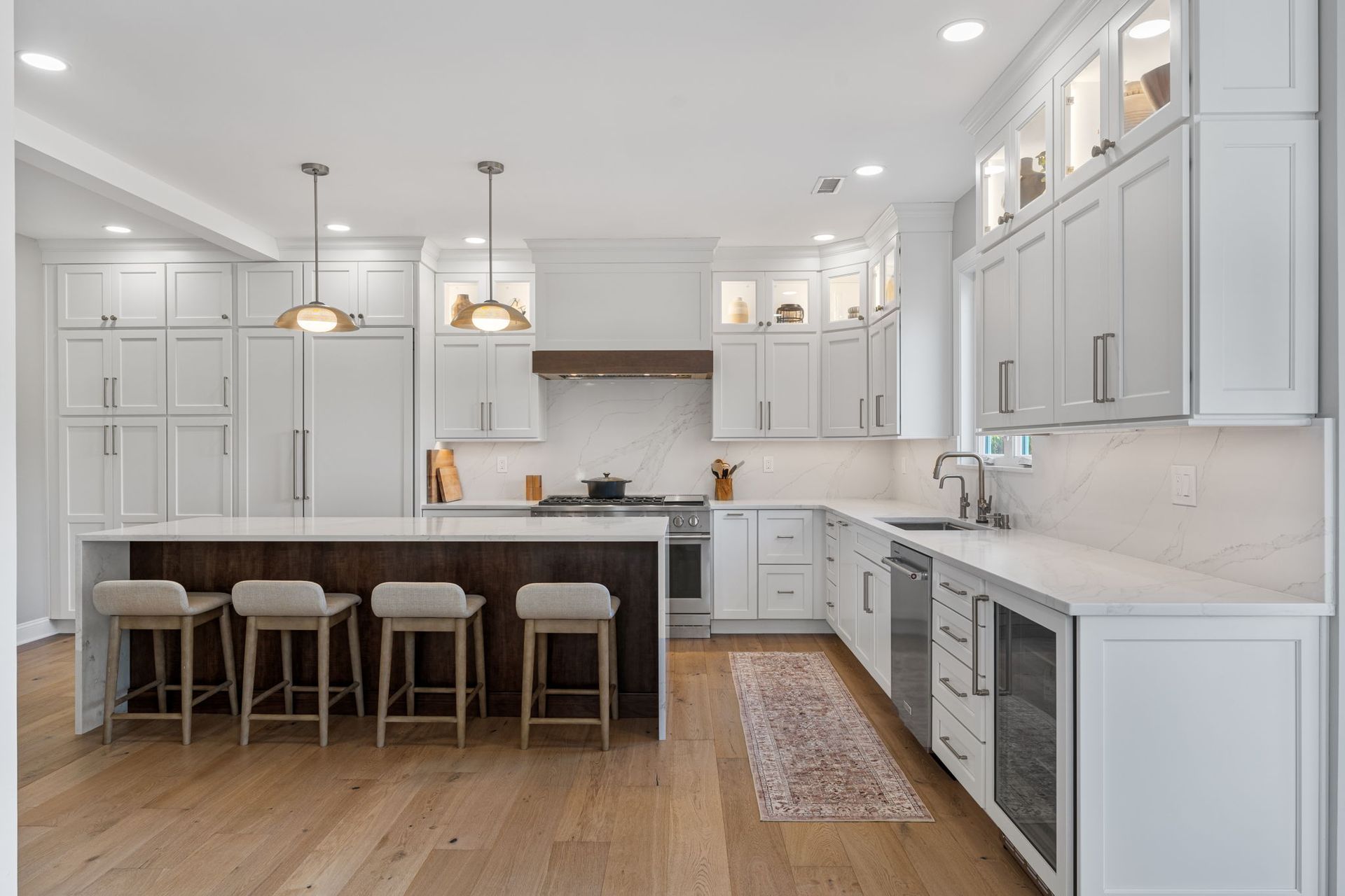 Bright white modern kitchen with island, barstools, wood floors, and stainless steel appliances In Bucks Country PA