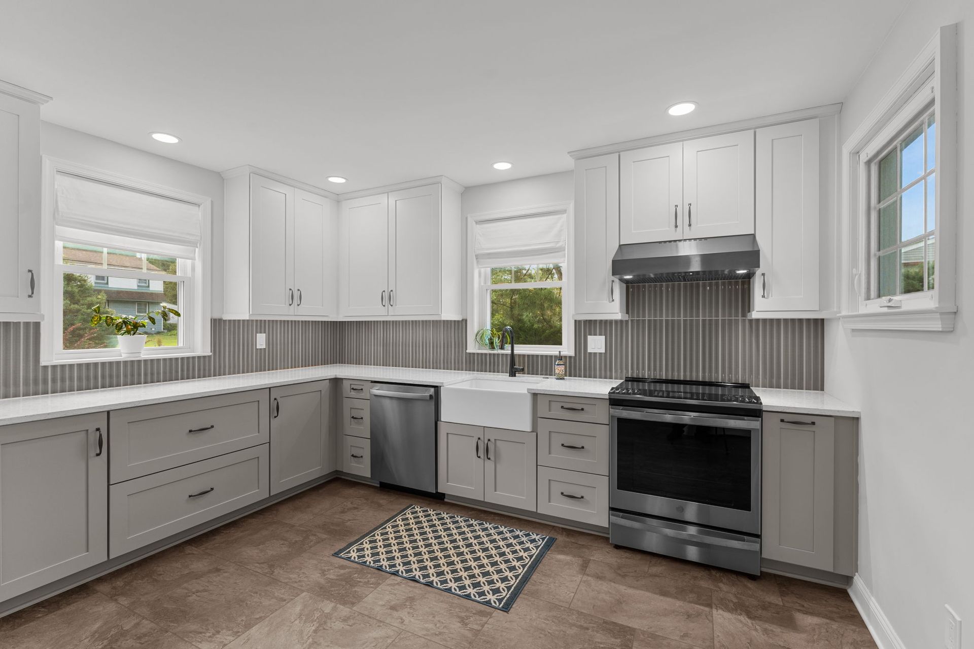 Bright modern kitchen with white cabinets, gray lower drawers, stainless appliances, and a patterned rug In Bucks County PA