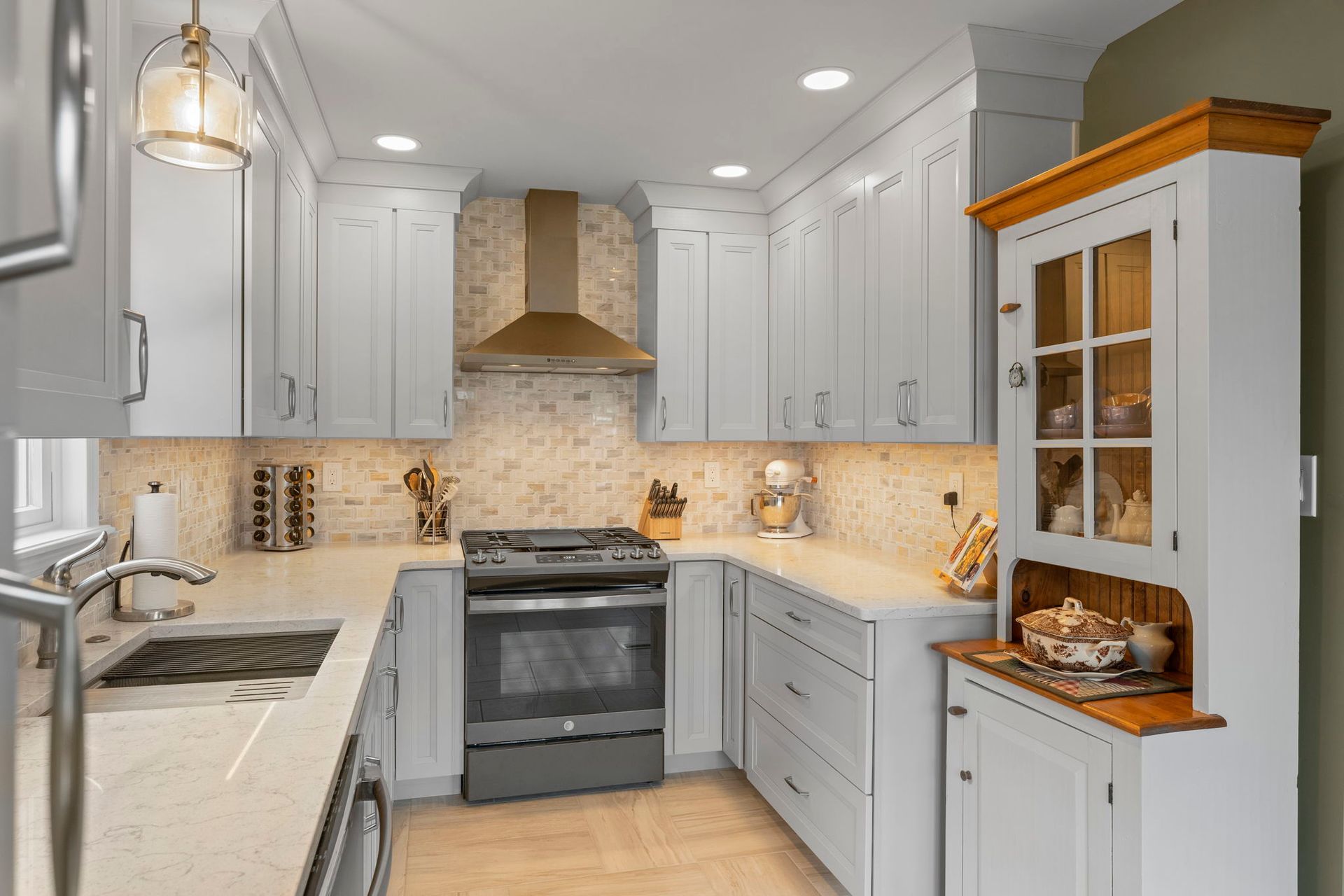 Bright modern kitchen with white cabinets, gray island, stainless stove, and warm tile backsplash In Bucks County PA