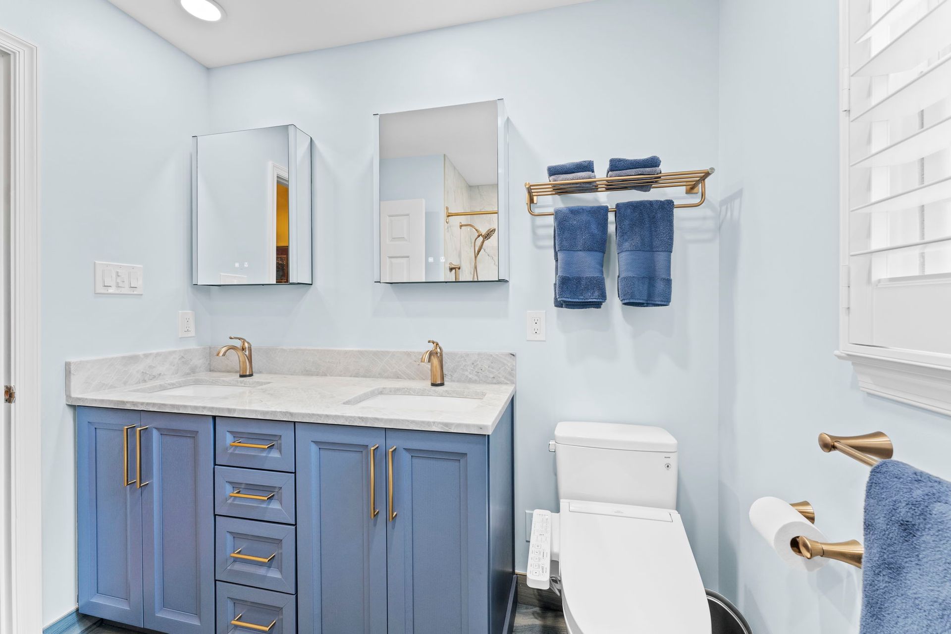 Bright blue bathroom with vanity, mirrors, toilet, and towel rack on light blue walls In Bucks County PA