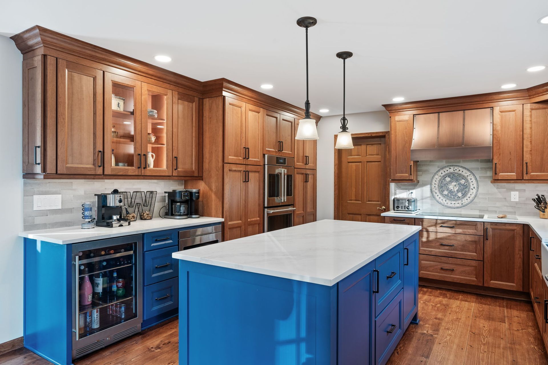 Bright kitchen with wood cabinets, white countertops, and a blue island under pendant lights In Bucks County PA