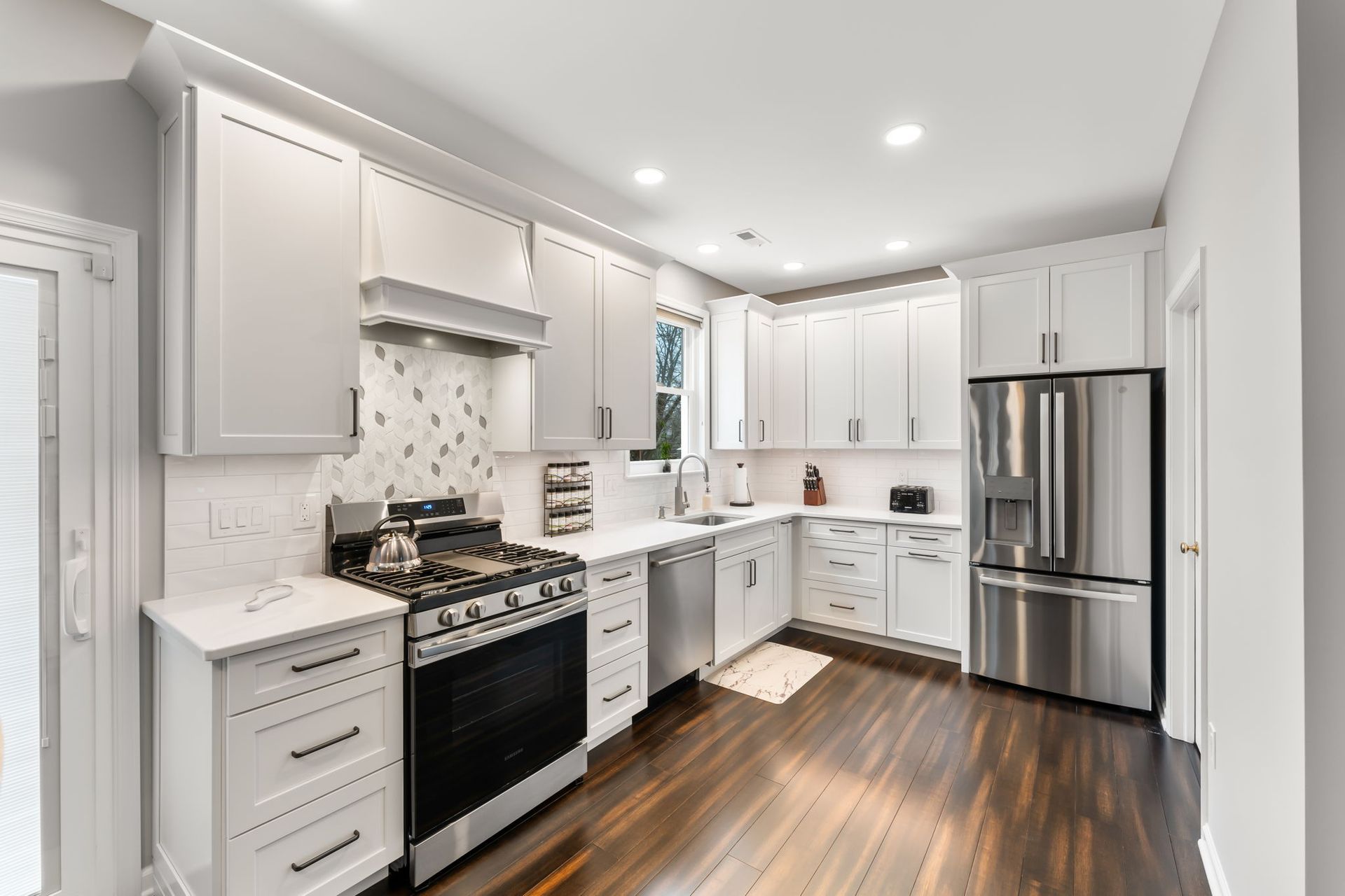 Bright white modern kitchen with stainless steel appliances, dark wood floor, and marble backsplash  In Bucks County PA