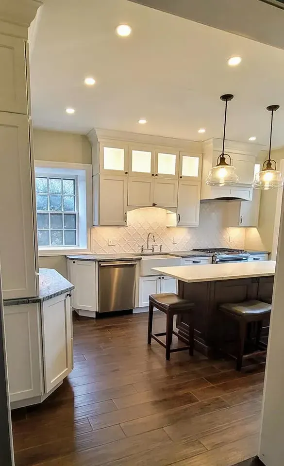 Bright modern kitchen with white cabinets, wood floors, island seating, and stainless steel appliances In Bucks Country PA
