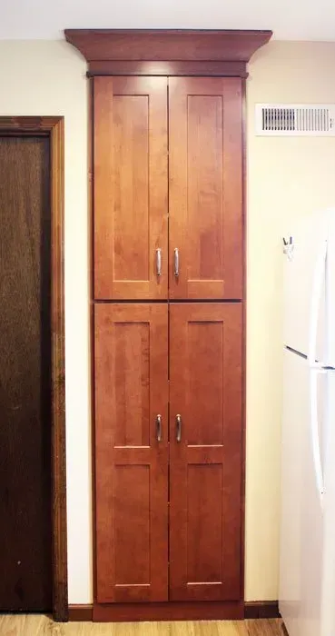 Tall wooden built-in cabinet with two doors in a hallway or kitchen alcove, framed by white walls  In Bucks County PA