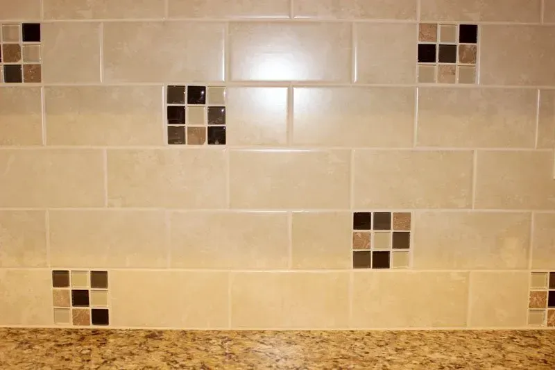 Beige tiled kitchen backsplash with small brown mosaic accents above a speckled granite counter  In Bucks County PA