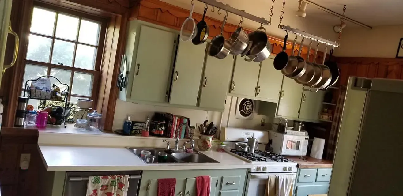 Cozy kitchen with hanging pots, white cabinets, and a large window over a counter In Bucks County PA