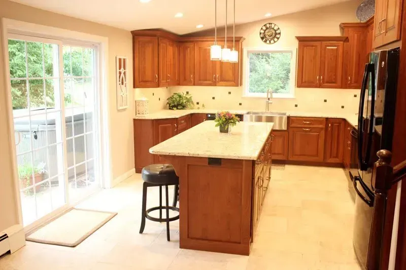 Bright kitchen with wood cabinets, island, black stool, stainless fridge, and sliding glass door to deck In Bucks Country PA