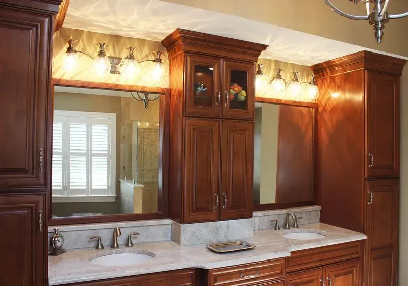 Wooden bathroom vanity with twin sinks, marble countertop, large mirror, and warm lighting  In Bucks County PA