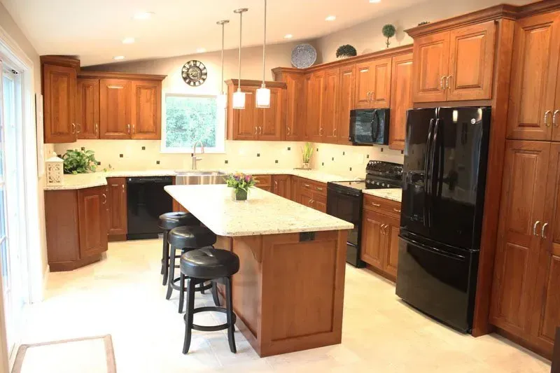 Bright wood kitchen with island, black stools, white countertops, and black appliances In Bucks County PA