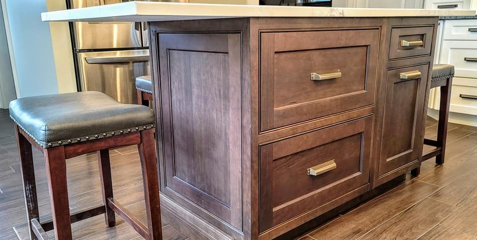 Wooden kitchen island with drawers beside a cushioned bar stool on a hardwood floor In Bucks County PA